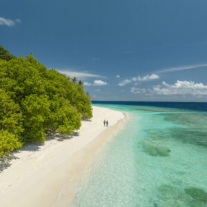 The woods of a Maldives tropical island, from a distance, with two small characters giving scale for the high drone angle of the tropical island.