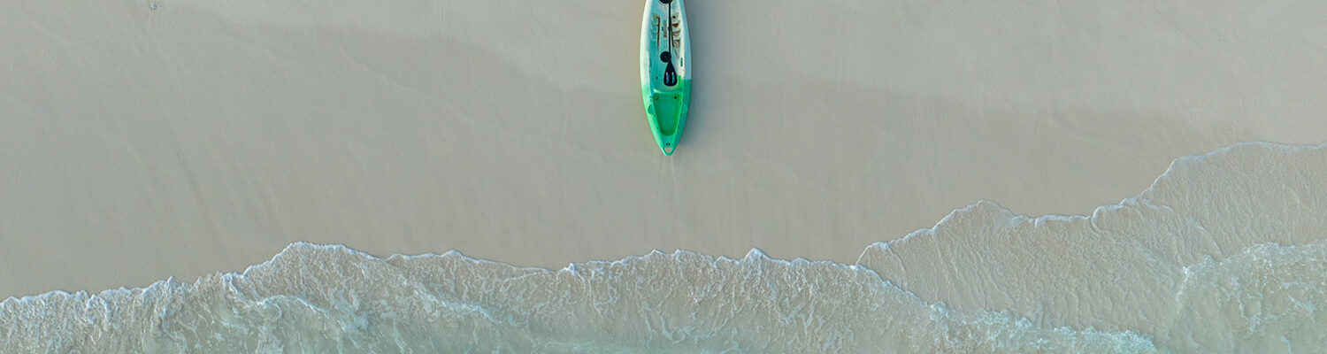 A canoe on a beautiful, clean beach with the water lapping at the shore.