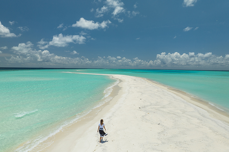 A lady walking along the idyllic sandbank with white sand and crystal clear water either side, on the island of Kamadhoo, Maldives.